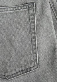 Szary materiał dżinsowy z pojedynczą tylną kieszenią ozdobioną poziomymi przeszyciami. Tekstura wydaje się gładka z delikatnym połyskiem.