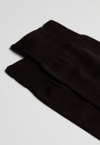 Sorte knæstrømper i højden med en tekstureret kant øverst, der har en glat finish og et let ribbet design. Lagt fladt ud på en lys baggrund.