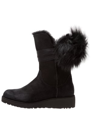 Botte d'hiver noire en daim mi-mollet avec garniture en fourrure et sangle décorative, semelle épaisse plate et détail en fourrure duveteuse à l'arrière.