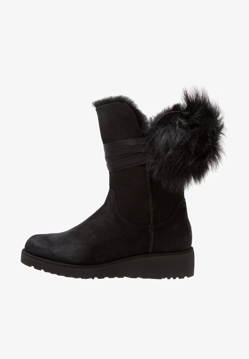 Botte d'hiver noire en daim mi-mollet avec garniture en fourrure et sangle décorative, semelle épaisse plate et détail en fourrure duveteuse à l'arrière.