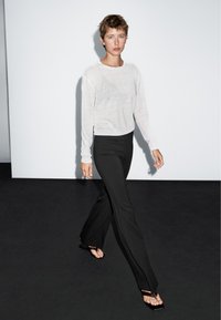 Leichtes, transparentes weißes Langarmshirt kombiniert mit eng anliegenden schwarzen Schlaghosen und schwarzen Sandalen mit offenen Zehen; einfache und glatte Texturen.