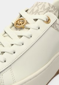 Sneaker in pelle bianca con motivo beige testurizzato sul tallone, dettaglio logo tono oro e lacci bianchi. Suola piatta in gomma.