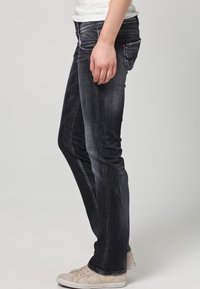 Vaqueros de lavado oscuro con un corte ajustado, que presentan un diseño de pierna recta. Están hechos de denim con un ligero desgaste, con estilo de cinco bolsillos y costuras visibles.