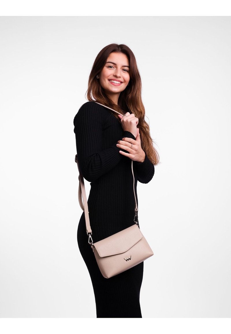 Béžová crossbody taška s texturovaným povrchem. Má přehnutý klopový víko a nastavitelné ramínko. Jednoduchý design s metalickým logem jako akcent.