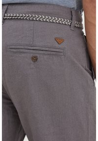 Grå shorts med ett vävt bälte med silverdetaljer, bakficka med knappstängning och en brun logotags.