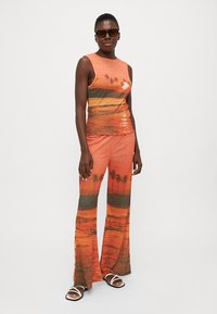 Conjunto de dos piezas que presenta una blusa sin mangas y pantalones acampanados. Tela naranja con un estampado de atardecer y palmeras. Textura suave, ajuste informal.
