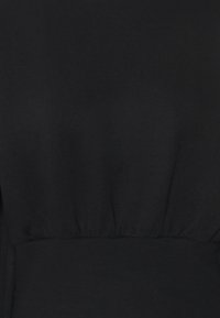 Tela negra en primer plano con una textura suave y un detalle fruncido en la cintura, con un color uniforme y sin patrones ni acentos visibles.