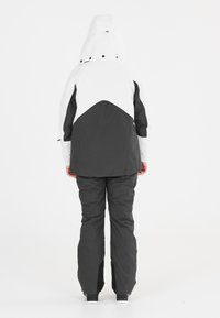 Bicolor jack in wit en donkergrijs met een capuchon, voorzien van een geometrisch ontwerp op de achterkant. Gecombineerd met bijpassende donkergrijze broek.