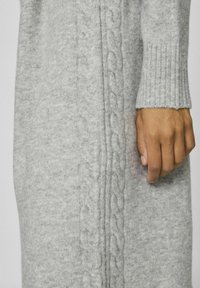 Pull gris en maille avec un motif torsadé sur le côté, poignets côtelés et texture douce. Coupe ajustée.