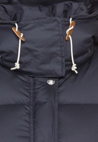Chaqueta de plumón azul marino con un cuello alto, cordones blancos, toggles de madera y un cierre de presión metálico en la parte delantera. Textura suave y acolchada.