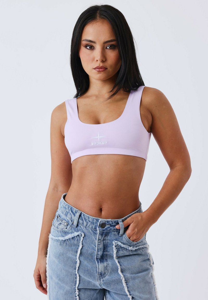 Sujetador deportivo en color lila con tirantes anchos y escote redondeado, con un logotipo bordado en blanco. Combinado con pantalones cortos de mezclilla azul desgastados.