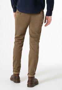 Brown cotton chinos with a textured pattern, slim fit, featuring rolled cuffs and a back pocket detail, paired with brown leather boots.