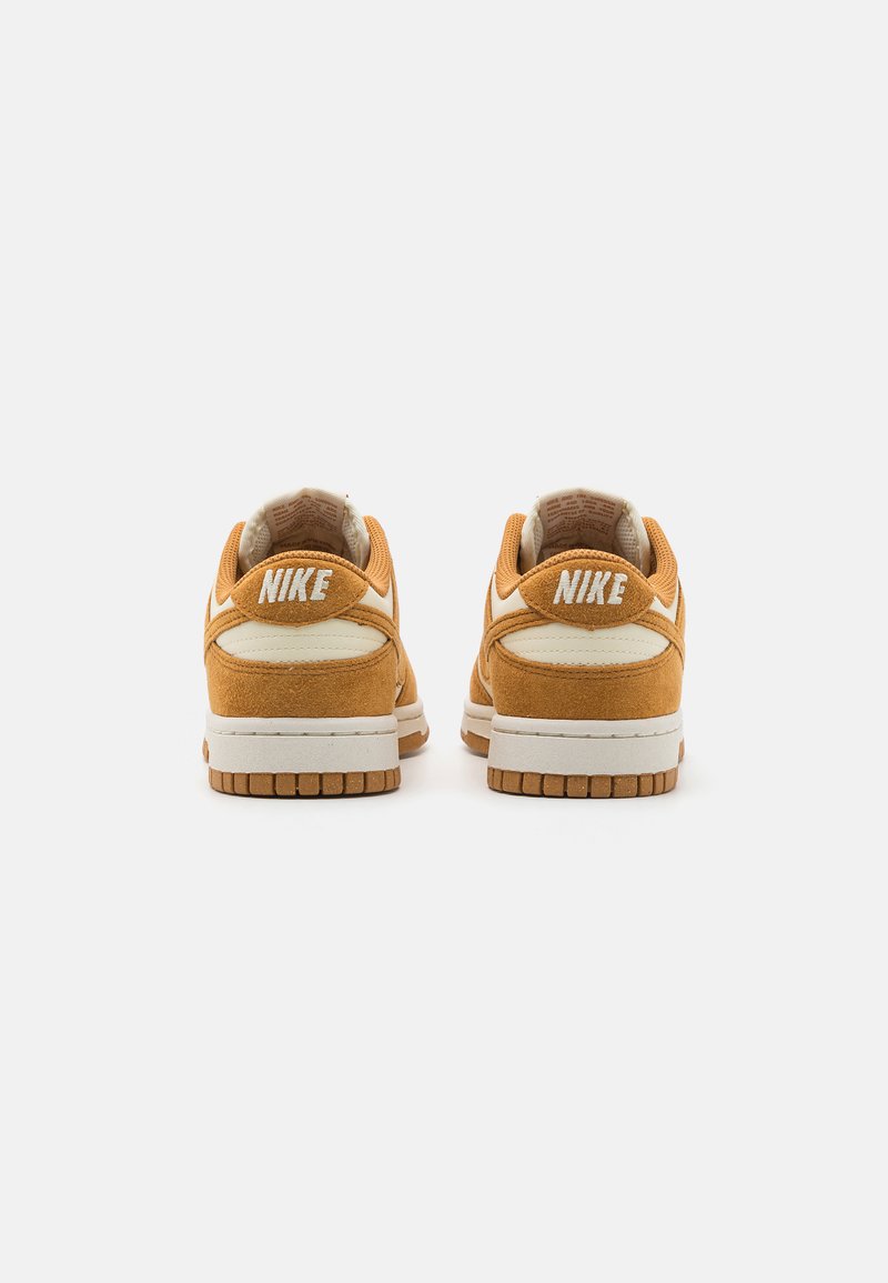 Baskets Nike Dunk en daim orange avec des accents blancs, col rembourré et semelle extérieure en caoutchouc texturé. Présente le logo 'NIKE' au niveau du talon.