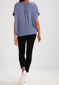 Lyseblå, løstsiddende top med tekstureret stof, korte ærmer og afrundet kant, kombineret med sorte slim-fit bukser og hvide sneakers.