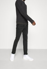 Ciemnoszary sweter z dzianiny z długimi rękawami, zestawiony z czarnymi obcisłymi dżinsami i białymi sneakersami, prezentujący casualową i nowoczesną sylwetkę.