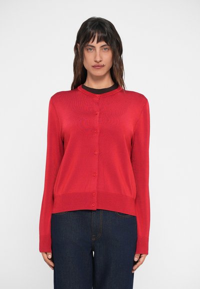 Red cardigan, buttoned front, round neckline, ribbed cuffs, and hem. Lightweight texture, worn over a dark shirt, paired with dark denim.