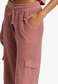Różowe, teksturowane spodnie dresowe z elastycznym pasem i sznurkiem, wyposażone w boczne kieszenie oraz kieszeń cargo na nogawce.