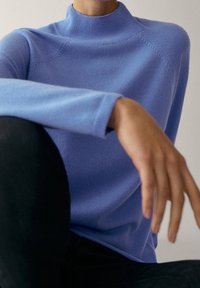 Pullover col roulé bleu clair avec un col côtelé et des manches longues, présentant une coupe décontractée et une texture douce.