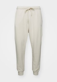 Krémově zbarvené tepláky z měkké látky s tahem v pase, žebrovanými manžetami a malým logem na boku.