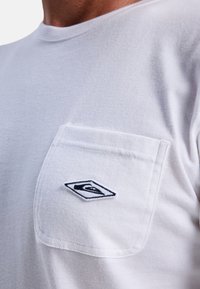 Hvid bomulds T-shirt med rund halsudskæring og en brystlomme med et sorte broderet logo i diamantform. Blød tekstur.