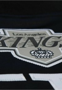 Schwarzer Stoff mit einem Logo-Patch der Los Angeles Kings in Grau und Schwarz, mit gestickten Details und einem Krone-Akzent.