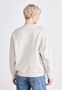 Light beige oversized sweatshirt with a round neckline, ribbed cuffs, and hem, featuring a smooth, soft texture and casual design.