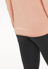 Langærmet, ribbet lyserød sportstrøje med en reflekterende kant ved kanten, parret med sorte leggings, der fremhæver rene linjer og strækbart stof.