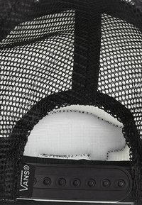 Casquette trucker noire en mesh avec une sangle snapback ajustable et une étiquette de la marque Vans visible à l’intérieur au-dessus de la visière.