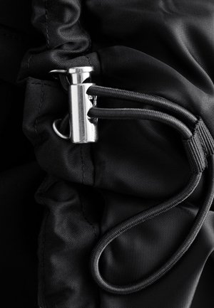 Metal cord lock securing two black elastic drawstrings on gathered black fabric.