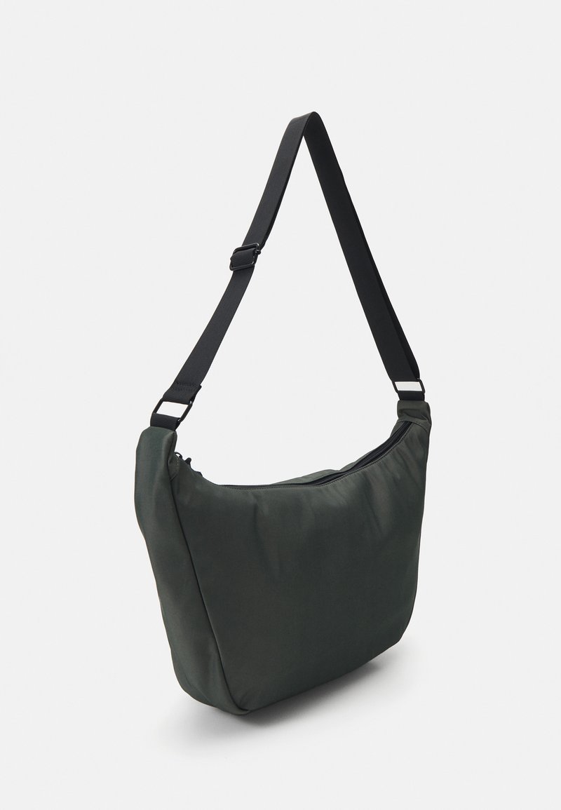 Bolso de hombro de nylon verde con una textura suave, forma redondeada y correa negra ajustable, que cuenta con un cierre de cremallera en la parte superior.