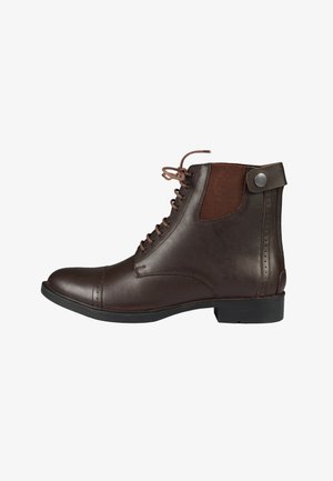 Bota tobillera de cuero marrón oscuro con cierre de cordones en la parte delantera, panel elástico en el lateral y correa con botón en la parte trasera sobre suela negra.