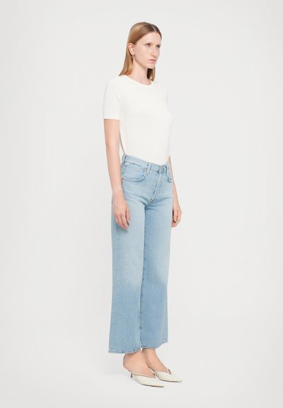 T-shirt aderente bianca leggera abbinata a jeans a gamba larga azzurri con vita alta, caratterizzati da un orlo grezzo e comodi décolleté.