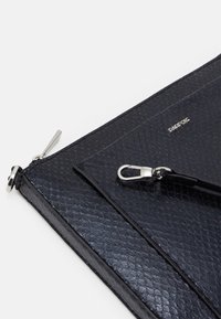 Borsetta in pelle nera con texture, dotata di accessori in argento, chiusura con zip e tracolla rimovibile. Logo del marchio posizionato sulla superficie.