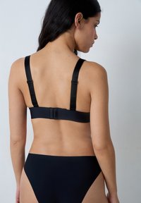 Soutien-gorge noir avec une texture lisse, des bretelles réglables et une fermeture à l'arrière. S'accorde avec des culottes taille haute noires. Design simple.
