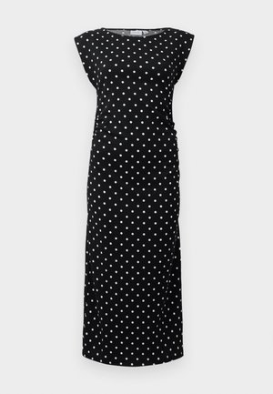 Robe noire avec des pois blancs, manches courtes, détails froncés sur le côté et une silhouette longue et ajustée. Fabriquée en tissu doux.