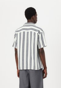 Camisa de manga corta con rayas verticales en azul marino y blanco, cuello y corte relajado. Fabricada en una tela ligera y texturizada.