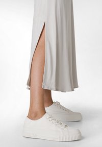 Robe longue gris clair, à la cheville, avec une fente sur le côté ; assortie à des baskets en toile blanches avec des semelles texturées et des lacets. Tissu lisse tombant subtilement.