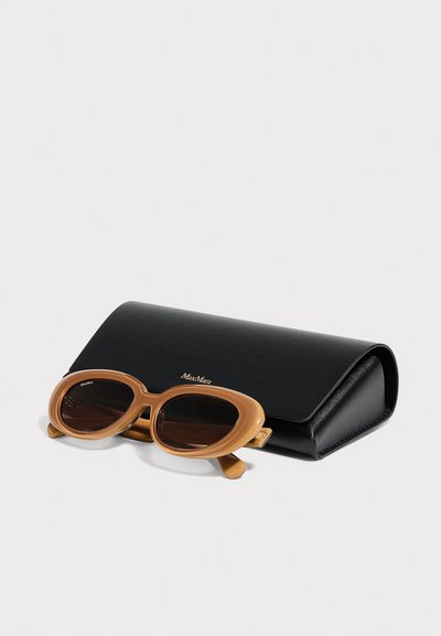 Lunettes de soleil ovales marron avec verres foncés reposant devant un étui rigide noir de la marque Max Mara sur fond blanc.