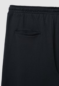 Schwarze Hosen aus strukturiertem Stoff, mit elastischem Bund und einer kleinen, flachen Tasche auf der rechten Seite.