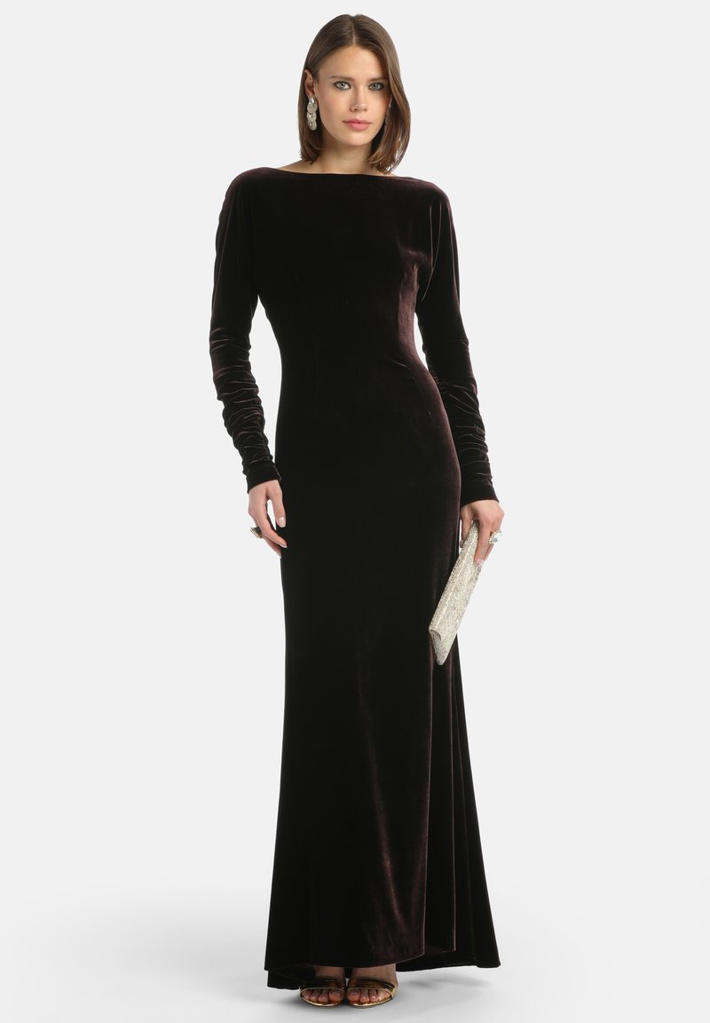 Ilga rankovėmis kadifo vakarinė suknelė tamsiai burgundiškoje spalvoje su prigludusia siluetu. Ją puošia laivagalio iškirptė ir subtili skeltė, derinama su sidabriniu rankiniu krepšiu.