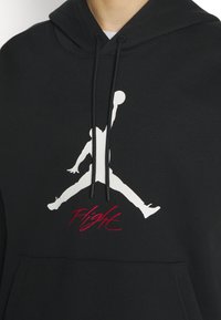 Sweat à capuche noir avec silhouette blanche d'un joueur de basketball sautant et tenant un ballon, avec le texte rouge "Flight" en dessous de la figure.