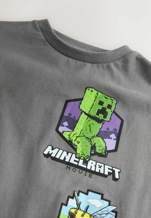 Grå bomulds T-shirt med et grafisk print af en grøn figur og teksten "MINECRAFT MOVIE" på en lilla hexagonal baggrund.