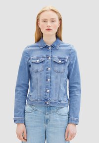 Chaqueta de mezclilla azul con un diseño ajustado, cierre de botón, dos bolsillos en el pecho y mangas largas. Detalles de costura distintivos en toda la prenda.