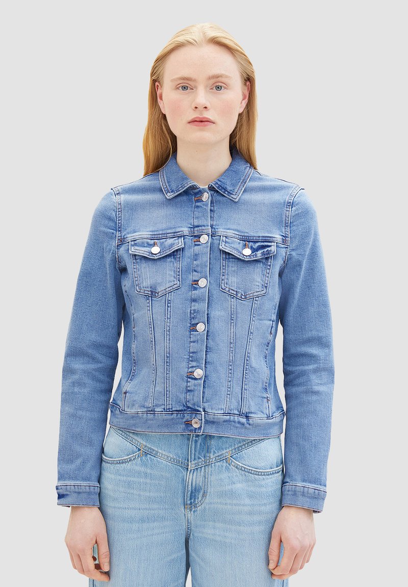Chaqueta de mezclilla azul con un diseño ajustado, cierre de botón, dos bolsillos en el pecho y mangas largas. Detalles de costura distintivos en toda la prenda.