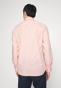 Camicia a maniche lunghe rosa chiaro con polsini a bottone, tessuto liscio, colletto e orlo curvo, vista da dietro.