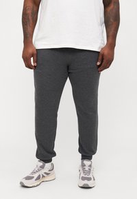 Grijze joggingsbroeken van zacht materiaal met een taps toelopend ontwerp, elastische boorden en een comfortabele pasvorm, gecombineerd met lichtgrijze sneakers.