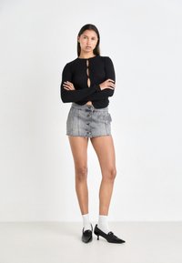 Top noir à manches longues avec trois découpes en forme de trou de serrure, associé à une mini-jupe en denim grise avec fermeture à boutons sur le devant et ourlet effiloché.