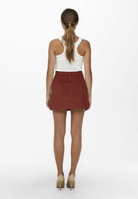 Minifalda de pana roja con corte recto, cintura alta y detalles en el bolsillo trasero, combinada con una camiseta sin mangas blanca y tacones beige.