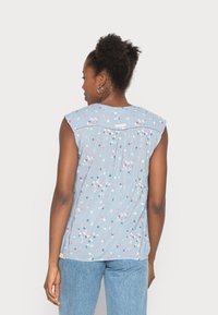 Top sem mangas de cor azul clara com padrão floral em rosa, branco e azul. Apresenta um fundo pregado e costura decorativa ao longo do decote.