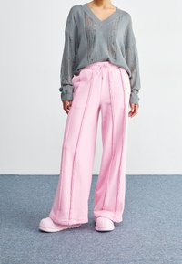 Ljusrosa vida sweatpants med dragsko i midjan och sidstygn, kombinerat med en lös grå V-ringad tröja.